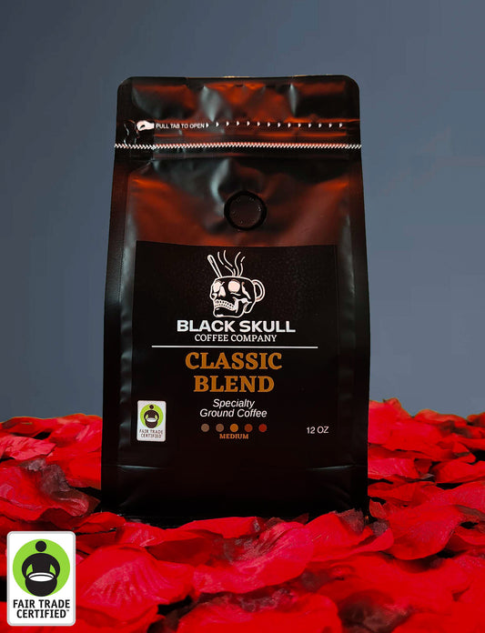 Black Skull Coffee Company Specialty Classic Blend Coffee 12oz ground coffee package on a gray background with red rose petals and Fair Trade USA Logo.