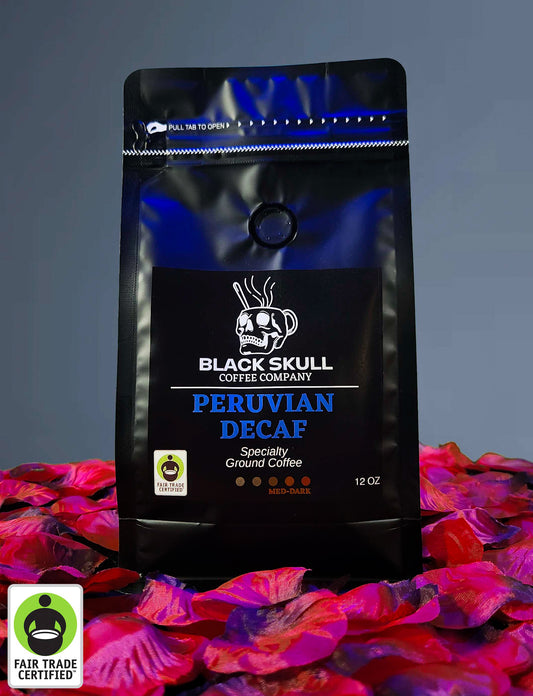 Black Skull Coffee Company Specialty Peruvian Decaf Coffee 12oz ground coffee package on a gray background with red rose petals and Fair Trade USA Logo.
