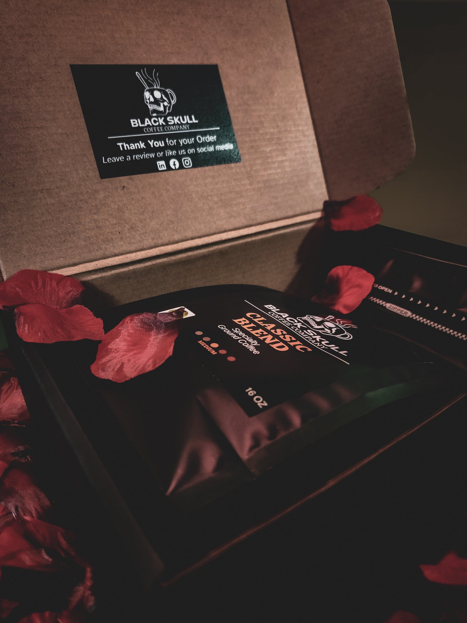 Black skull-themed coffee bag with a brown box and red flower petals.