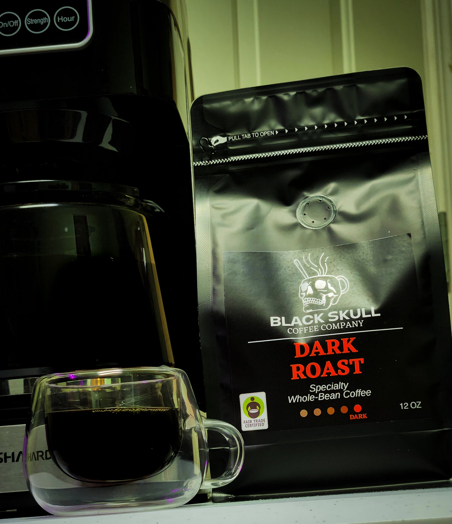 Black Skull Coffee Company Dark Roast coffee package with a glass of coffee in front of a coffee machine.