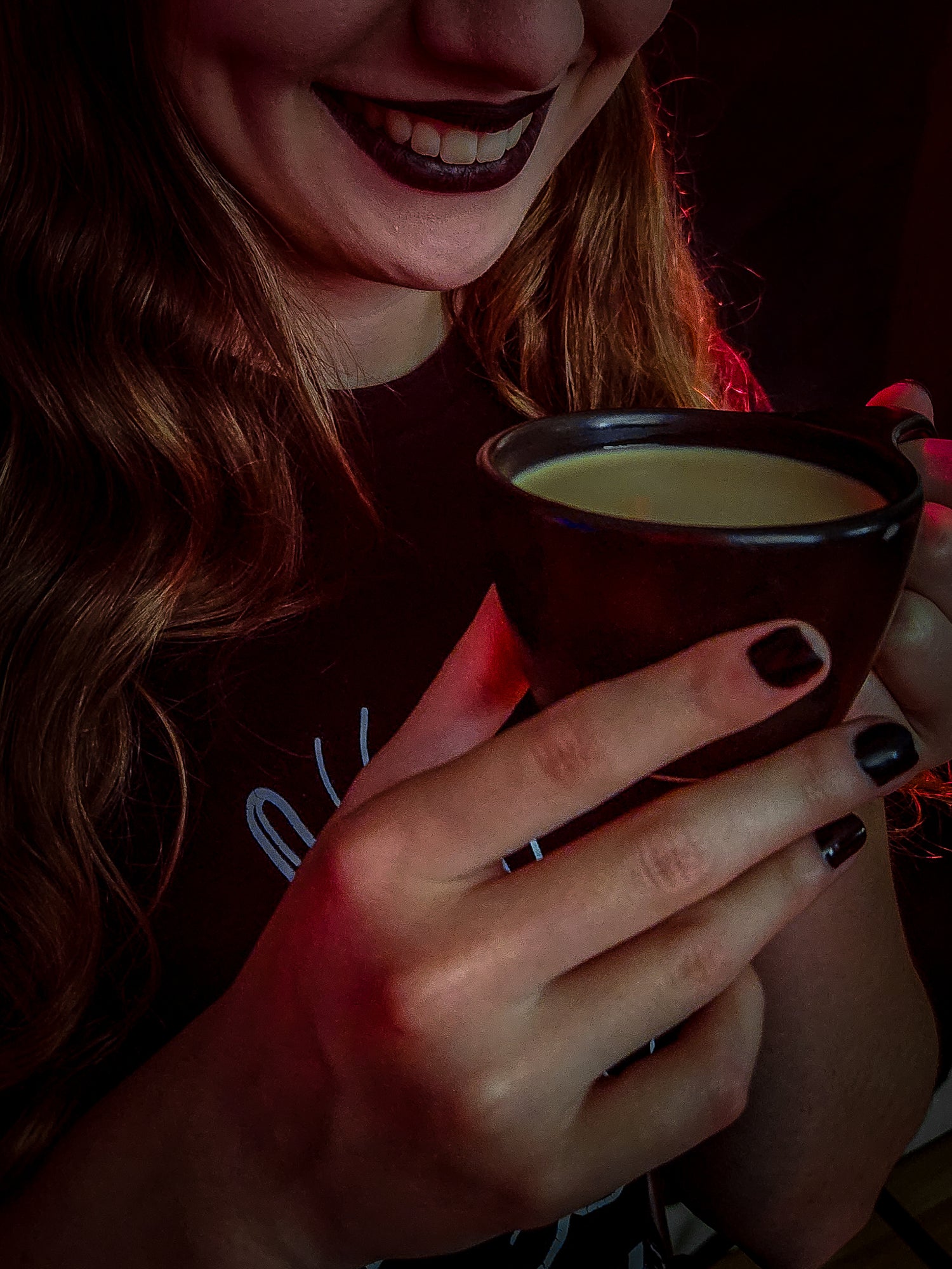 Person wearing Black Skull Coffee Company shirt holding a small coffee cup with a dark background